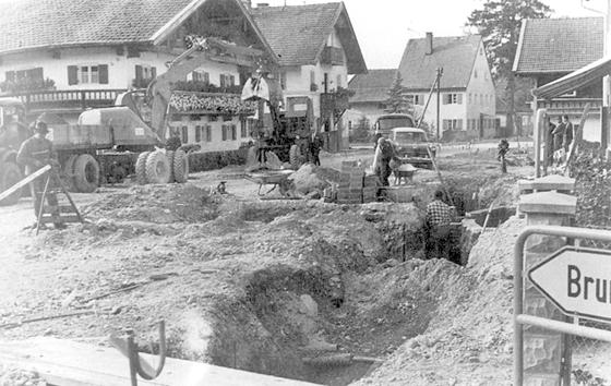 Erdarbeiten beim Ausbau der Rosenheimer Straße an der Brunnthaler Straße im Jahr 1965. Im Hintergrund das Pfarrhaus. 	Quelle: Ortschronik Höhenkirchen