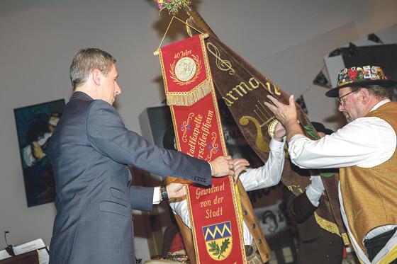 Bürgermeister und Schirmherr Christoph Böck befestigt das Jubiläumsband an der Fahne der Stadtkapelle.	Foto: VA