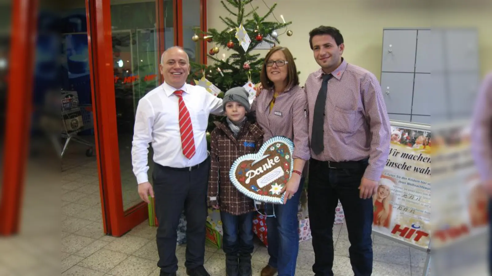 Marktleiter Selim Spanjolli, der 8-jährige Sebastian, Monika Forster, die die Aktion betreut, und der stellvertretende Marktleiter Mustafa Yolcu (v.l.) hoffen auf viele Kunden, die eine Wunschkarte vom Baum pflücken und den Kinderwunsch erfüllen. (Foto: HIT Pasing)