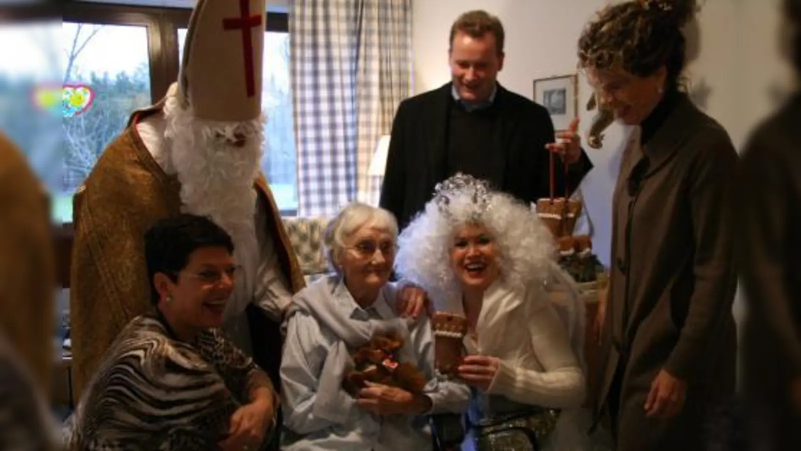 Sie sorgten für einen stimmungsvollen Nikolaustag in St. Gisela: Kurt Mory als Heiliger Nikolaus, Peter Köstler, Sibylle Madadkar (hintere Reihe von links), Sonja Mayer, <br>und Brigitte Hartl als Engel (vorn von links) besuchten jeden Heimbewohner einzeln und verteilten ihre Gaben. Heimbewohnerin Susanne Bienefeld freute sich über die Aufmerksamkeiten. (Foto: US)