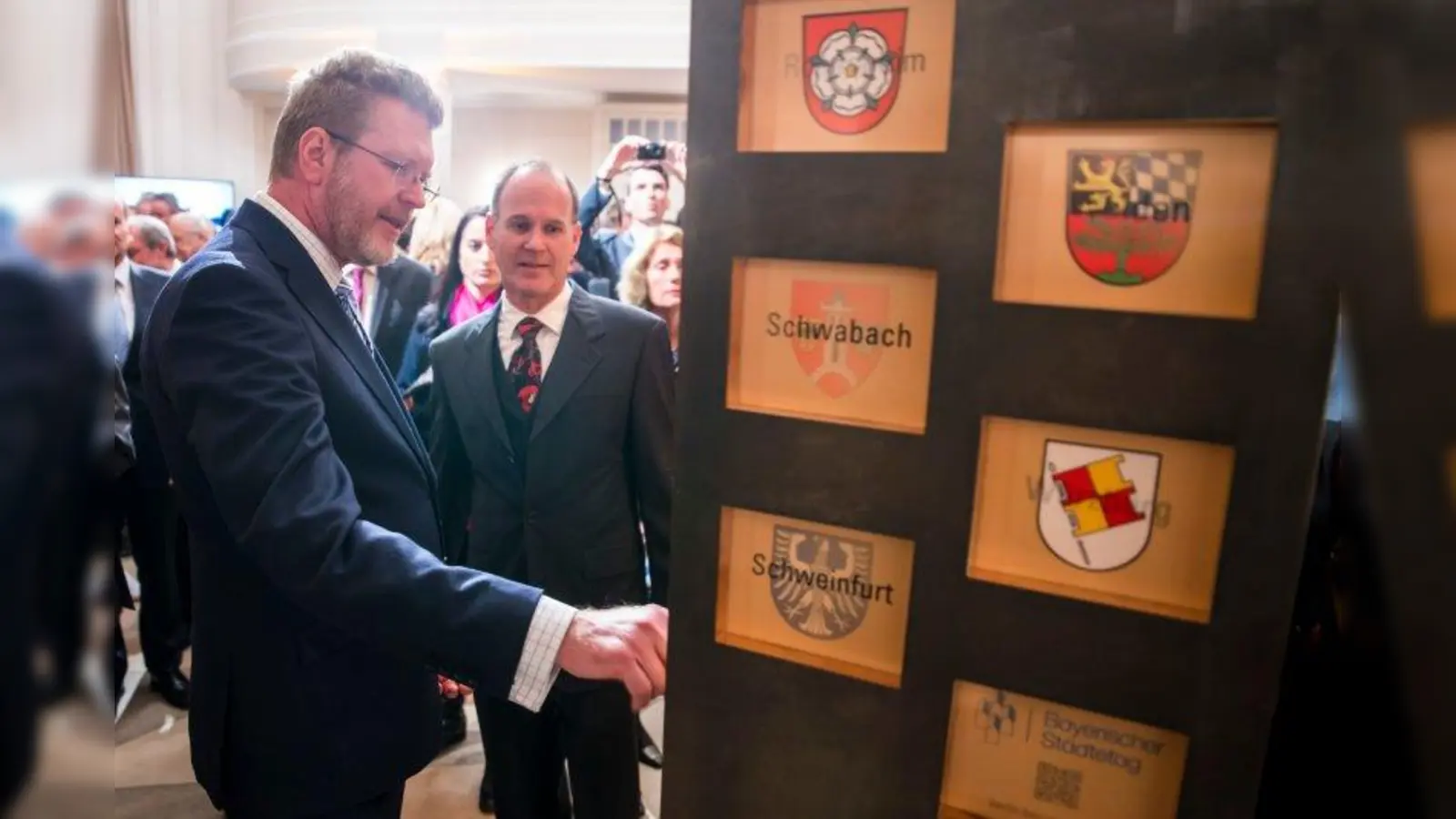 Die kreisfreien Städte Bayerns sind nun auch - dank drei Gautinger Künstler - sichtbar in der Bayerischen Vertretung in Berlin. Formforscher Peter Waller und Staatsminister Marcel Huber (v.l.) im Gespräch an der Wappenstele. (Foto: © Bayerische Staatskanzlei | Henning Schacht)