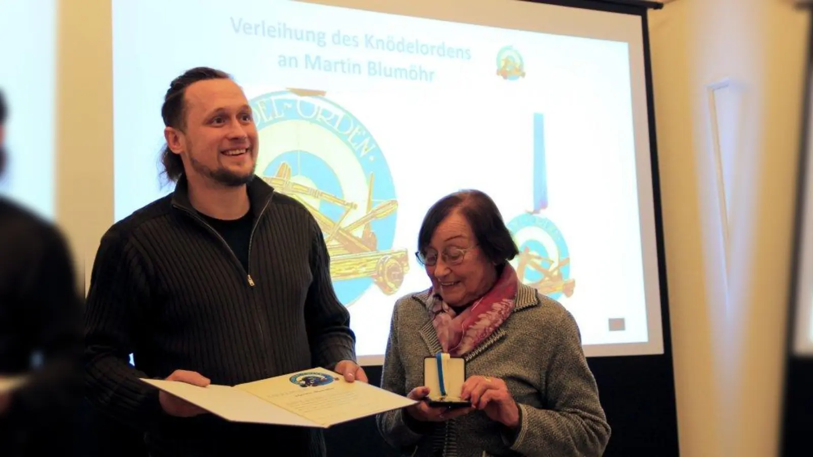 „Unter allen Geschichten, die ich bei meiner Tunnelarbeit und meiner Pasing-Recherche gehört habe, ist die von der Knödelschleuder mit Abstand die beeindruckendste.“ Maler Martin Blumöhr nimmt den Knödelorden von Elisabeth Winter entgegen. (Foto: us)