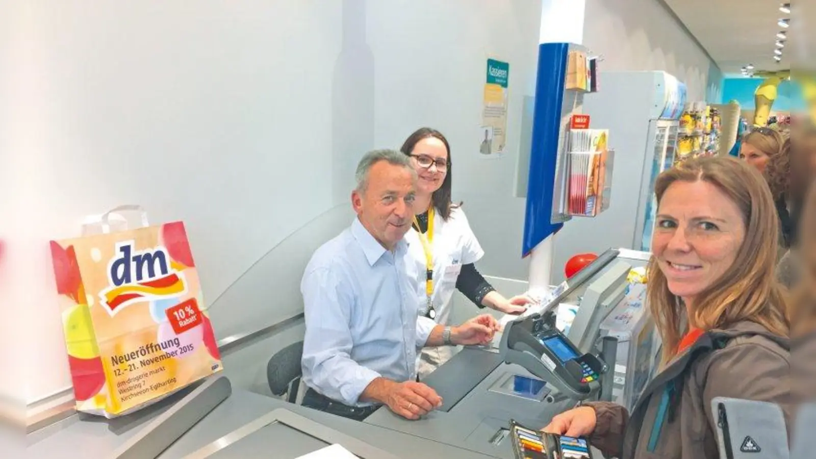 Bürgermeister Udo Ockel an der dm-Kasse, betreut von dm-Mitarbeiterin Sandra Scharf, mit einer dm-Kundin (Foto: dm)