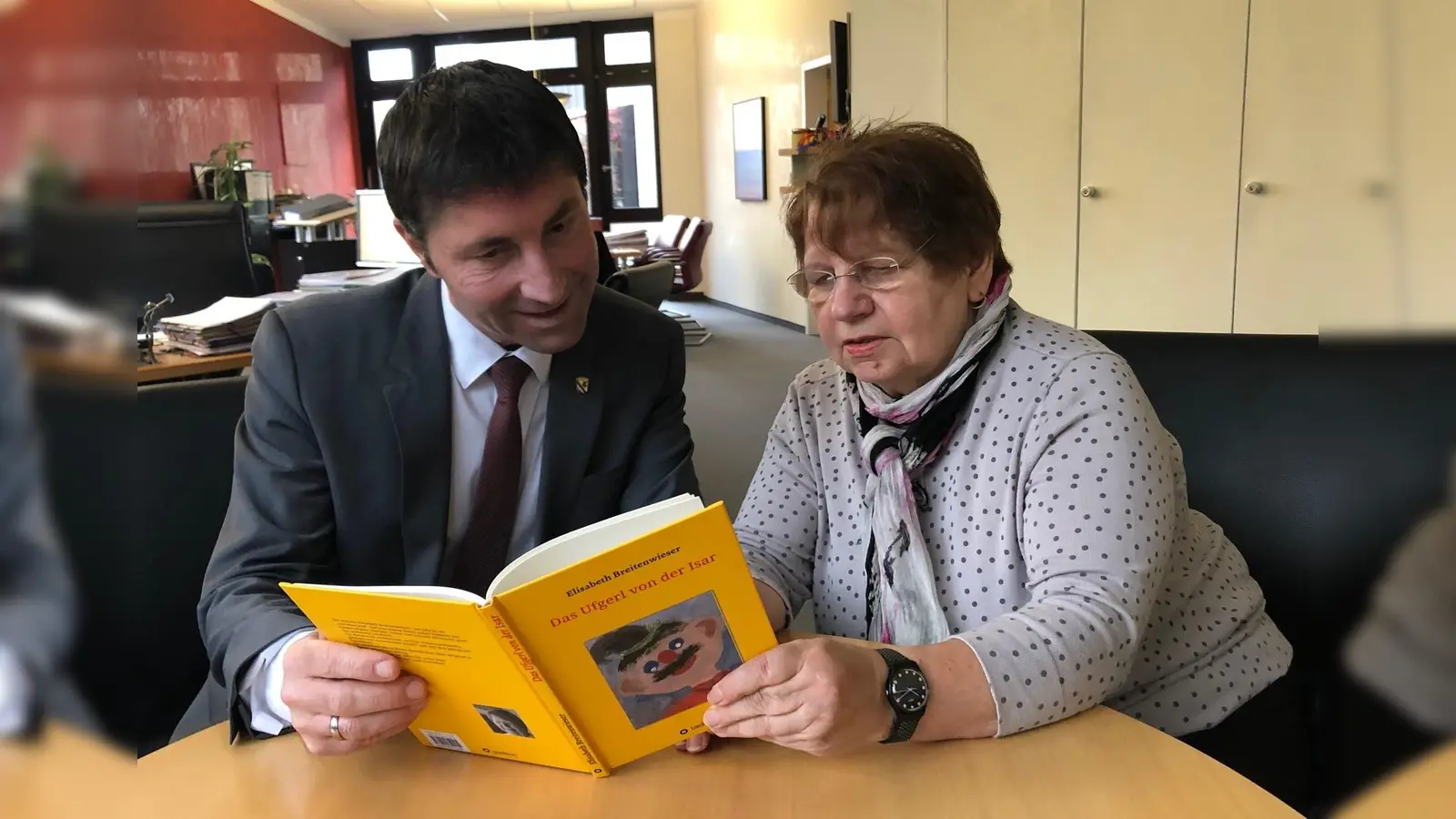 Unterföhrings Bürgermeister Andreas Kemmelmeyer durfte schon in das neue Buch vom Kobold „Ufgerl“ hineinschnuppern, das Elisabeth Breitenwieser nicht nur geschrieben, sondern auch illustriert hat. (Foto: Gemeinde UFG)