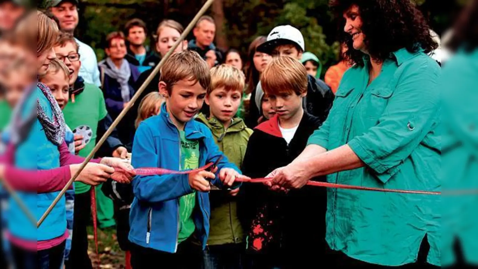 Phillip (8) durchschneidet als jüngster der »Zukunftsagenten« das rote Band zur Eröffnung, rechts daneben Schirmherrin Astrid Schweizer, Kinderbeauftragte des Bezirksausschusses 16. 	 (Foto: privat)