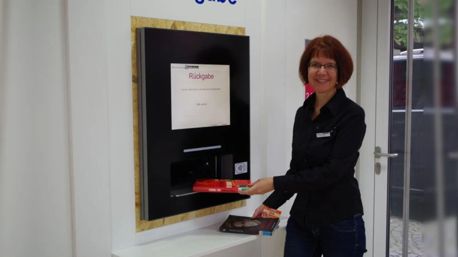 Ab jetzt können Bibliothekskunden in Laim ihre Bücher rund um die Uhr abgeben. Stefanie Zech demonstriert den neuen Rückgabeautomaten. (Foto: kö)