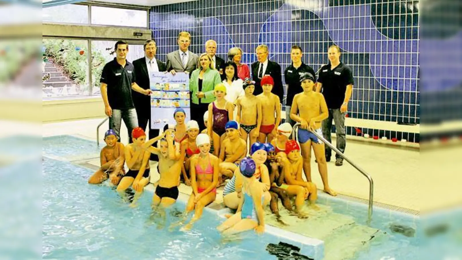 Staatssekretärin Melanie Huml (4.v.l.), Axel Kampmann von der Versicherungskammer Bayern (3.v.l), Stadtrat Christian Müller (2.v.l.) und Vertreter der DLRG überreichen den Kindern an der Grundschule an der Burmesterschule ein Baderegel-Plakat.	 (F.: VA)