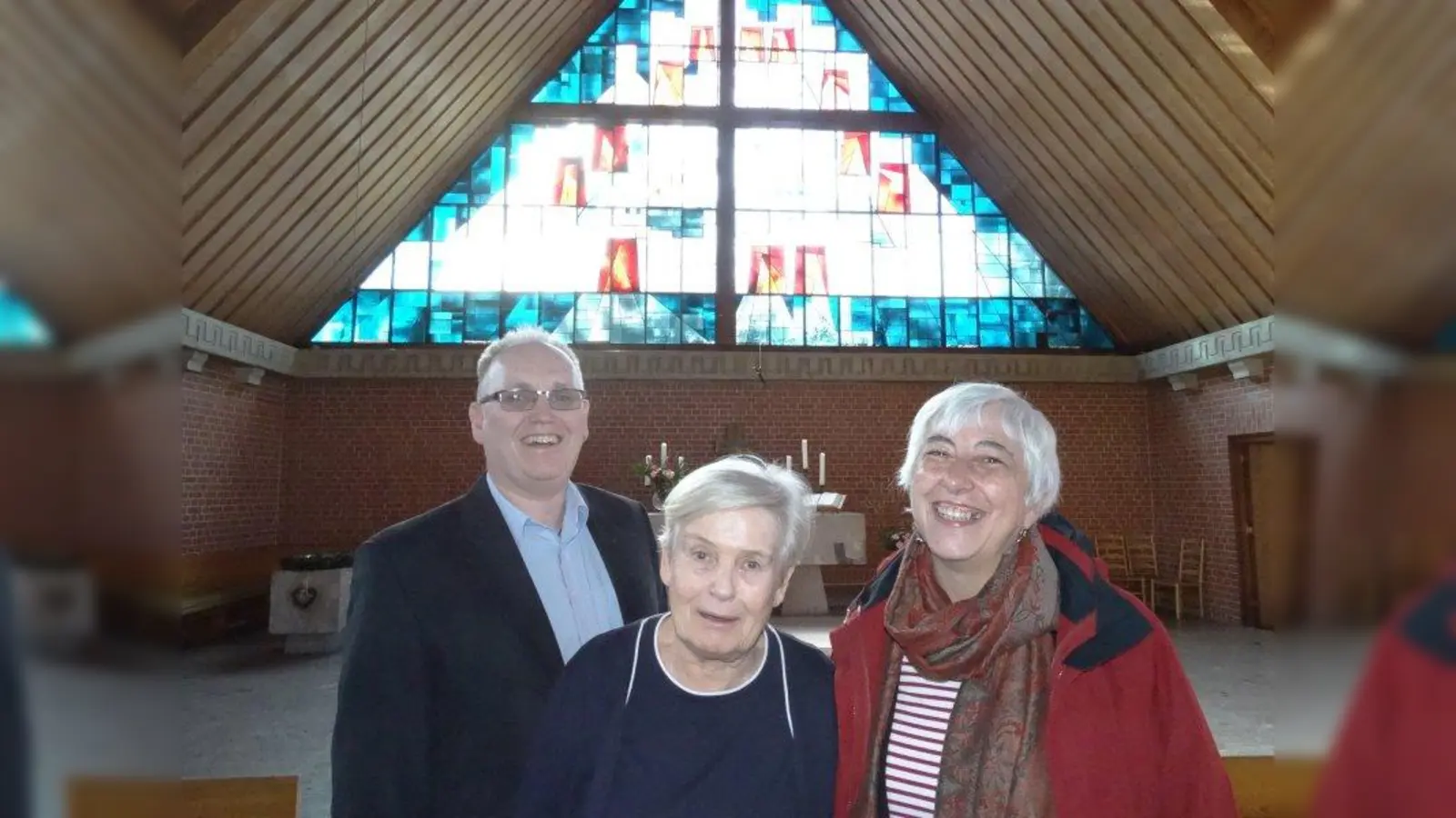 Pfarrer Michael Trimborn und die beiden Gemeindemitglieder Renate Rückert und Annemarie Heinrich (von links) im Innenraum der Reformations-Gedächtnis-Kirche. Im Hintergrund ist das dreieckige Giebelfenster zu sehen, das von der Künstlerin Angela Gsaenger gestaltet wurde. Ihr Vater Gustav Gsaenger war Architekt der Kirche. (Foto: tab)