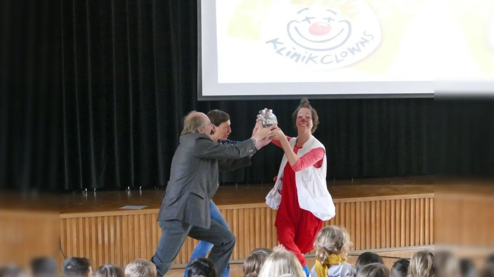 Schulleiter Friedrich Fichtner und Elternbeiratsvorsitzende Michaela Bacherl übergaben KlinikClown Fiderallala ein Glas voller Scheine und Münzen: 1683 Euro und 12 Cent. (Foto: ds)