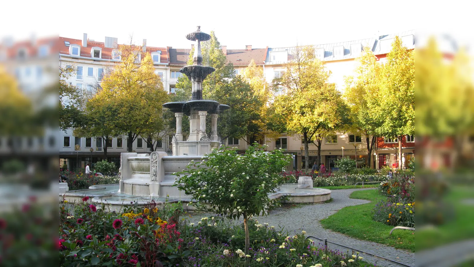 Der Glaspalastbrunnen inmitten von Blumenbeeten auf den Weißenburger Platz. (Foto: gemeinfrei)
