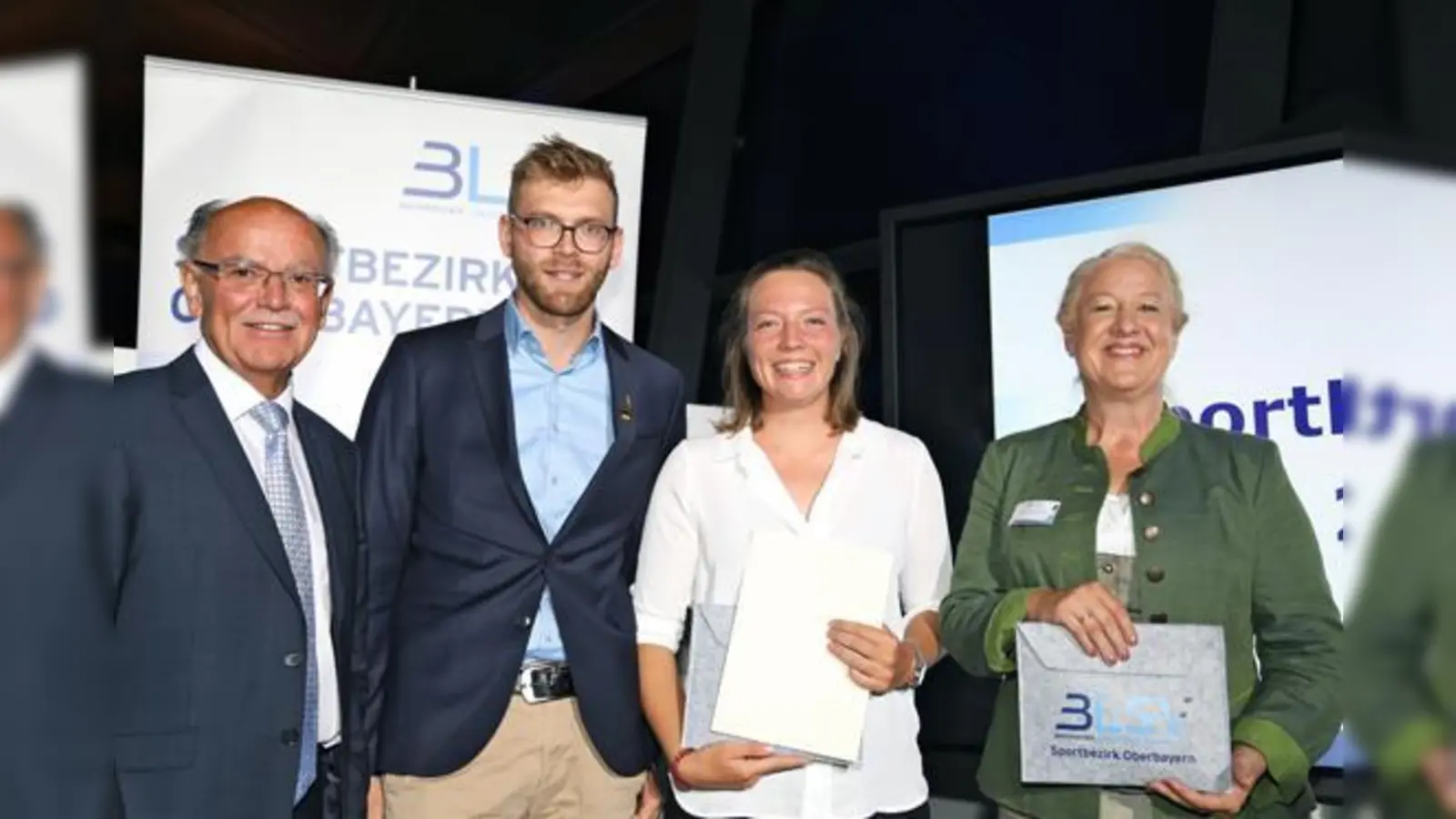 Bezirkstagspräsident Josef Mederer (l.) und Bezirksvorsitzende Claudia Daxenberger (r.) gratulieren Charlotte von Bockelmann und ihrem Trainer Lucas Artmann zur gewonnenen Auszeichnung.  (Foto: alpenPR)