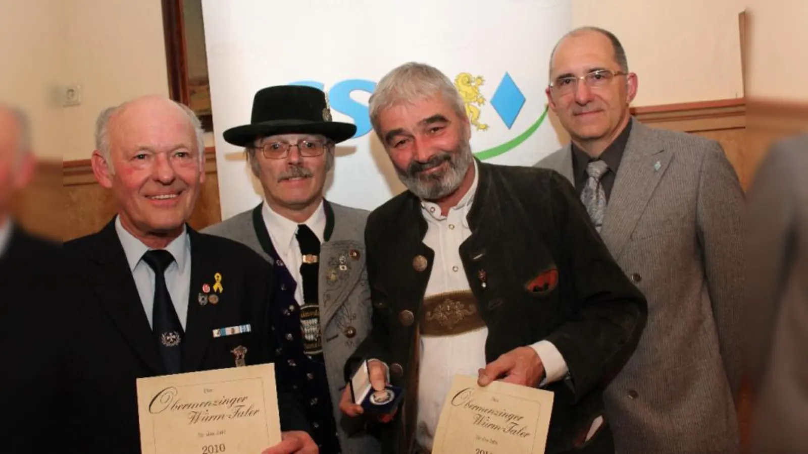 Karl Grandl, stellvertretend für den VKR Obermenzing, und Ulrich Grams (vorn v.l.) freuten sich über den Würmtaler Orden. Laudator Frieder Vogelsgesang lobte deren großes Herz für Obermenzing, Hans Menzinger zeigte Filme über das Wirken der Geehrten (hinten, v.r.). (Foto: US)