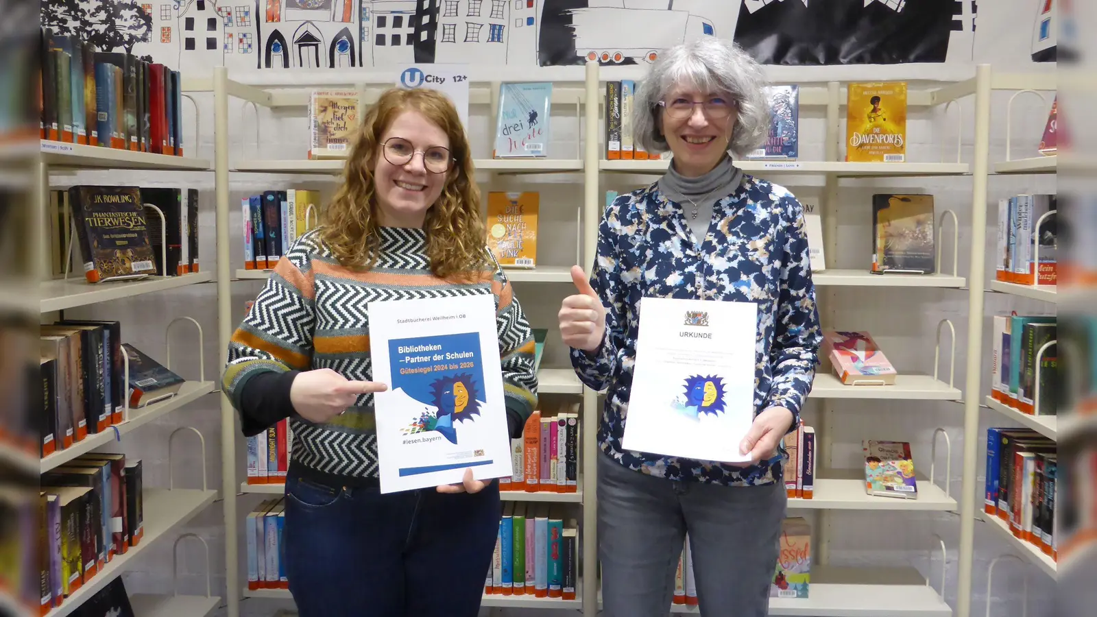 Ausgezeichnete Stadtbibliothek in Weilheim (von links): Sandra Knittel (stellv. Bibliotheksleitung) und Simone Groß (Bibliotheksleitung) präsentieren die Urkunde. (Foto: Stadtbücherei)