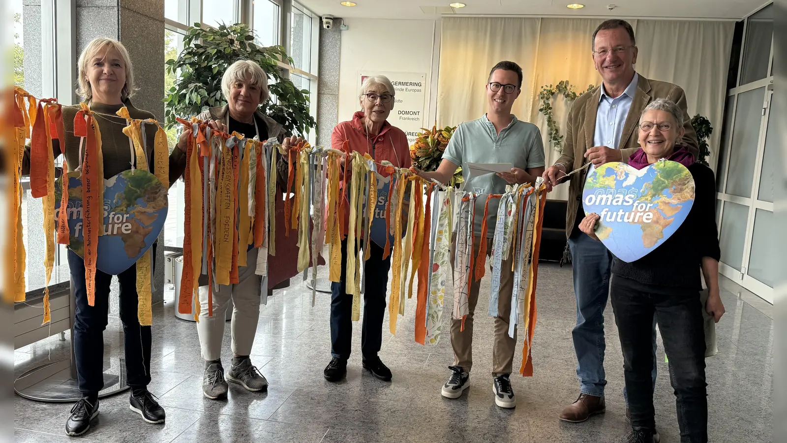 Die „Omas for Future” überreichen die Leine mit den Klimabändchen an Andreas Hass (r.) und Klimaanpassungsbeuftragten Christian Klöpfer. (Foto: pst)