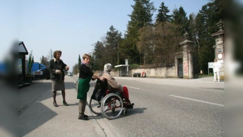 Ein sicherer Überweg über die befahrene Bergsonstraße kann noch dauern. Zwar hat das KVR den Zebrastreifen für „gleich nach den Osterferien“ versprochen, doch muss nun erst einmal ein gemeinsamer Ortstermin von VR, Baureferat und Straßenbeleuchtung gefunden werden. Auf die hilfsbereiten Helfer der Gärtnerei müssen die Querungswilligen also noch eine Weile zurückgreifen. V.l. Franziska Miroschnikoff, Gärtnerei-Mitarbeiterin Rita Straßl mit Kundin. (Foto: US)