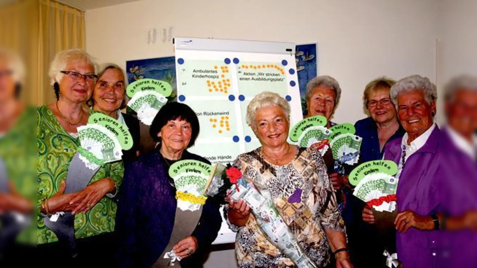 Stricken für den guten Zweck: Sieben Frauen präsentieren sich vor einem Plakat, auf dem die sieben Einrichtungen aufgelistet sind, die jeweils 1000 Euro durch die »strickenden Seniorinnen« erhalten haben. 	 (Foto: ws)
