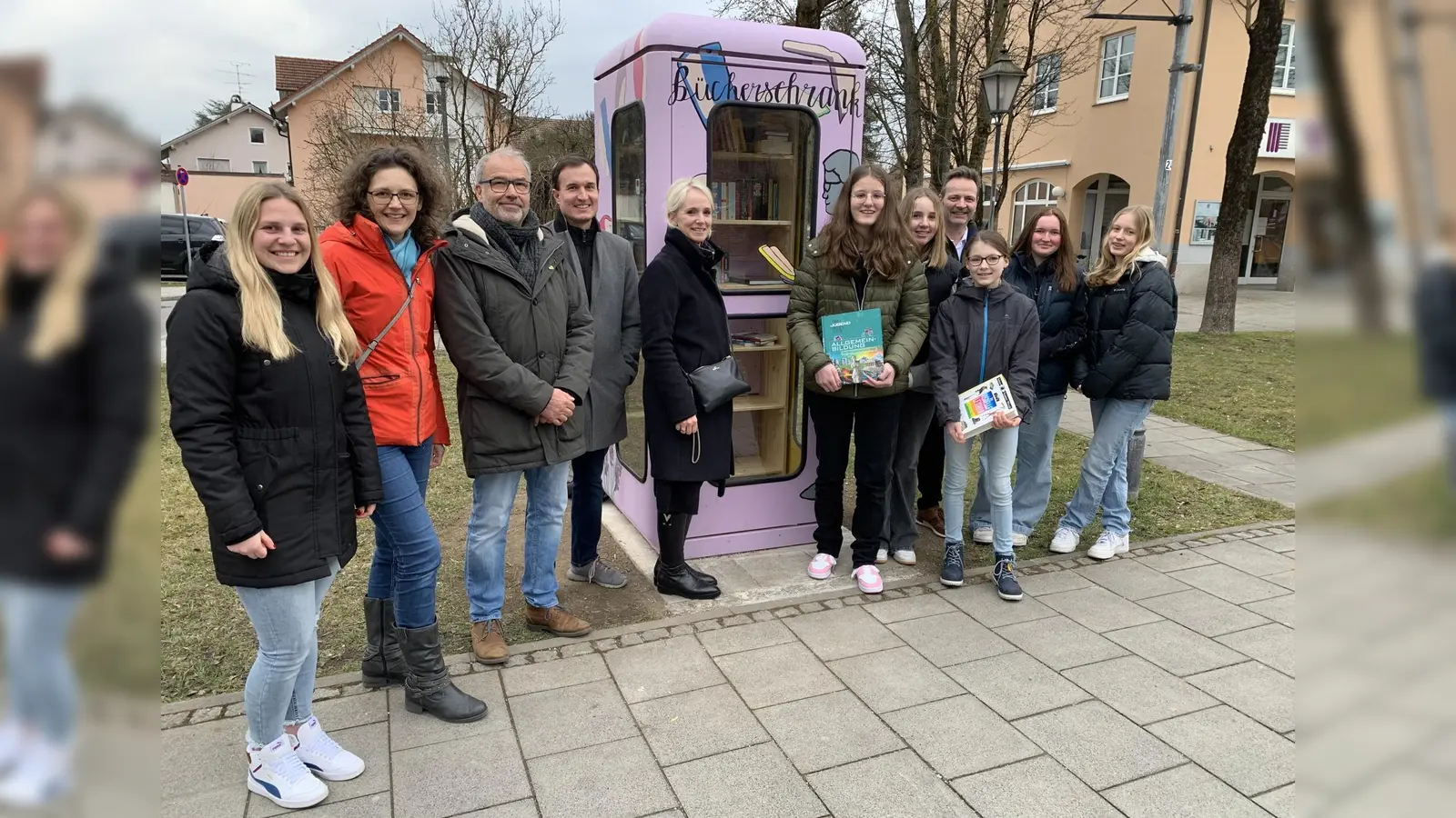 Über den neuen Bücherschrank in Aschheim freuen sich neben Vertreterinnen und Vertretern der Gemeinde auch die Schülerinnen der 8. Klasse des Kunstzweiges der St.-Emmeram-Realschule. (Foto: Gemeinde Aschheim)