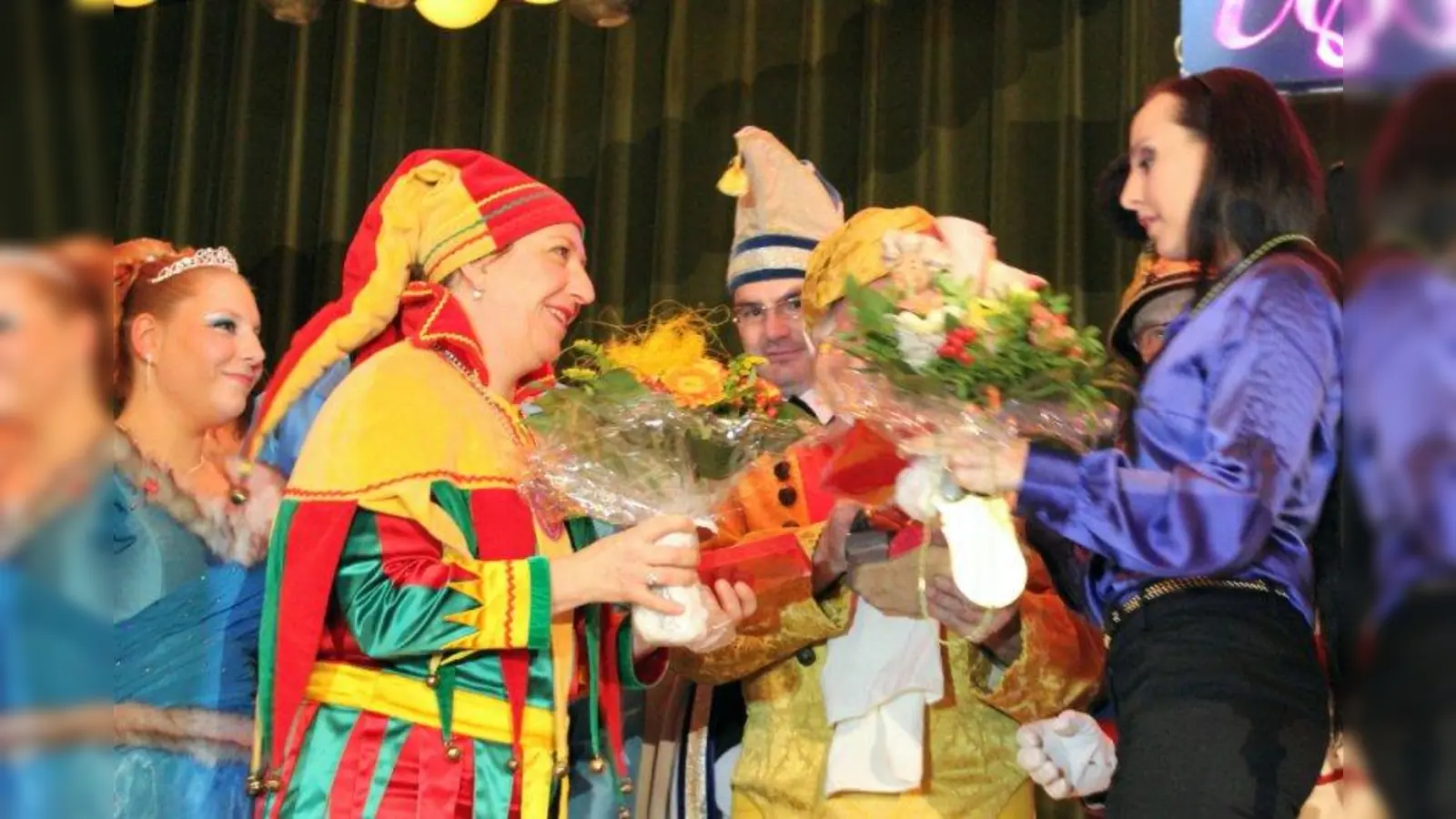 Zirkus und Fasching sind Seelenverwandte in Sachen Lebensfreude und Verwandlung: Hofnarr Regina übergibt Blumen und Jahresorden an die Juniorchefin des Zirkus Krone, Jana Mandana Lacey-Krone (v.l.). (Foto: US)