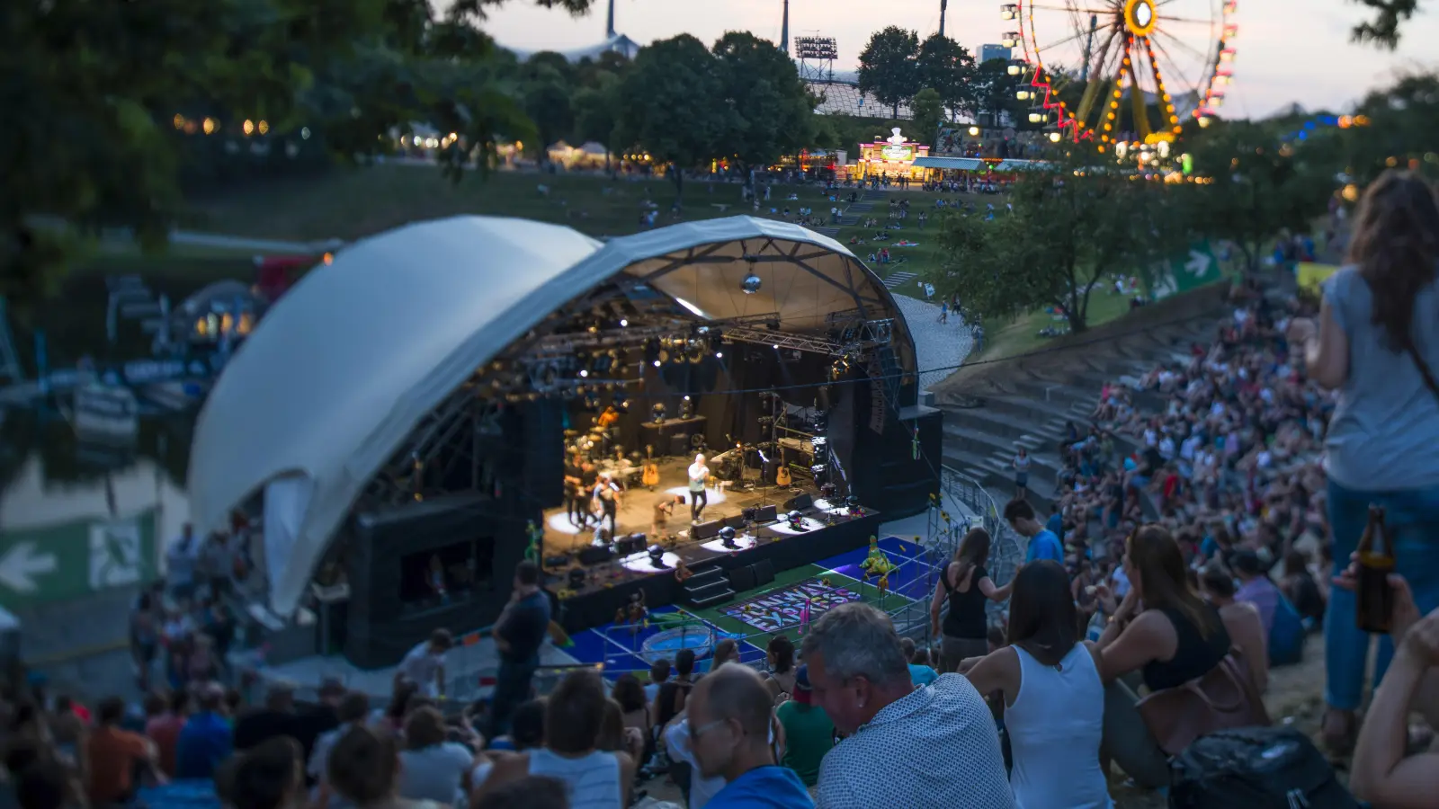 Im Olympiapark finden in August zeitgleich zwei tolle Veranstalungen statt: das Sommerfestival, von dem hier das Riesenrad zu sehen ist, und der kostenlose MusikSommer auf der Seebühne.  (F.: Martin Hangen/ Olympiapark München)