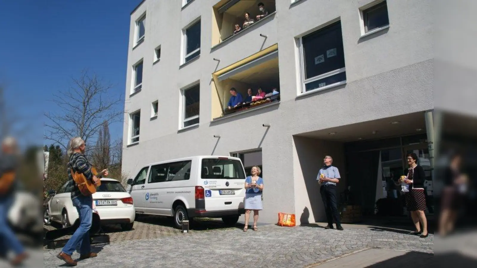Die Überreichung der Osterfladen vom Cafe am See aus Weßling mit musikalischer Einlage von Erik Berthold war eine willkommene Abwechslung für die „Barrierefrei-Musikanten”, die derzeit ihr Wohnheim der Lebenshilfe Starnberg nicht verlassen dürfen. Die „Barrierefrei-Musikanten” ist ein seit 2014 bestehendes Projekt unter der musikalischen Leitung von Erik Berthold für Menschen mit und ohne Behinderungen. Leider fallen derzeit alle Musikproben und Auftritte und auch die Arbeit in den entsprechenden Werkstätten für die Bewohner des Wohnheims aus. Auch der Bestand an Mundschutzmasken geht zu Ende, entsprechende Spenden sind hier willkommen und dringend nötig. Unser Bild zeigt (von links): Erik Berthold (mit Gitarre), Elisabeth Vass (Organisation), Christian Münzel (Pädagogischer Leiter), Edith Dieterle (Geschäftsführung) und die Barrierefrei-Musikanten (auf den Balkonen). (Foto: Kuttenberger)