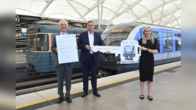 Konrad Schober (l.) mit der Inbetriebnahme-Genehmigung neben Ingo Wortmann, dem Deborah Schmitz (Siemens Mobility) einen symbolischen U-Bahn-Schlüssel überreicht. Sie präsentieren sich vor dem 85. C2-Zug und einem Zug der Serie A, die vom den C2-Zügen ersetzt wird. (Foto: SWM/ MVG)