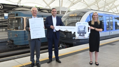 Konrad Schober (l.) mit der Inbetriebnahme-Genehmigung neben Ingo Wortmann, dem Deborah Schmitz (Siemens Mobility) einen symbolischen U-Bahn-Schlüssel überreicht. Sie präsentieren sich vor dem 85. C2-Zug und einem Zug der Serie A, die vom den C2-Zügen ersetzt wird. (Foto: SWM/ MVG)