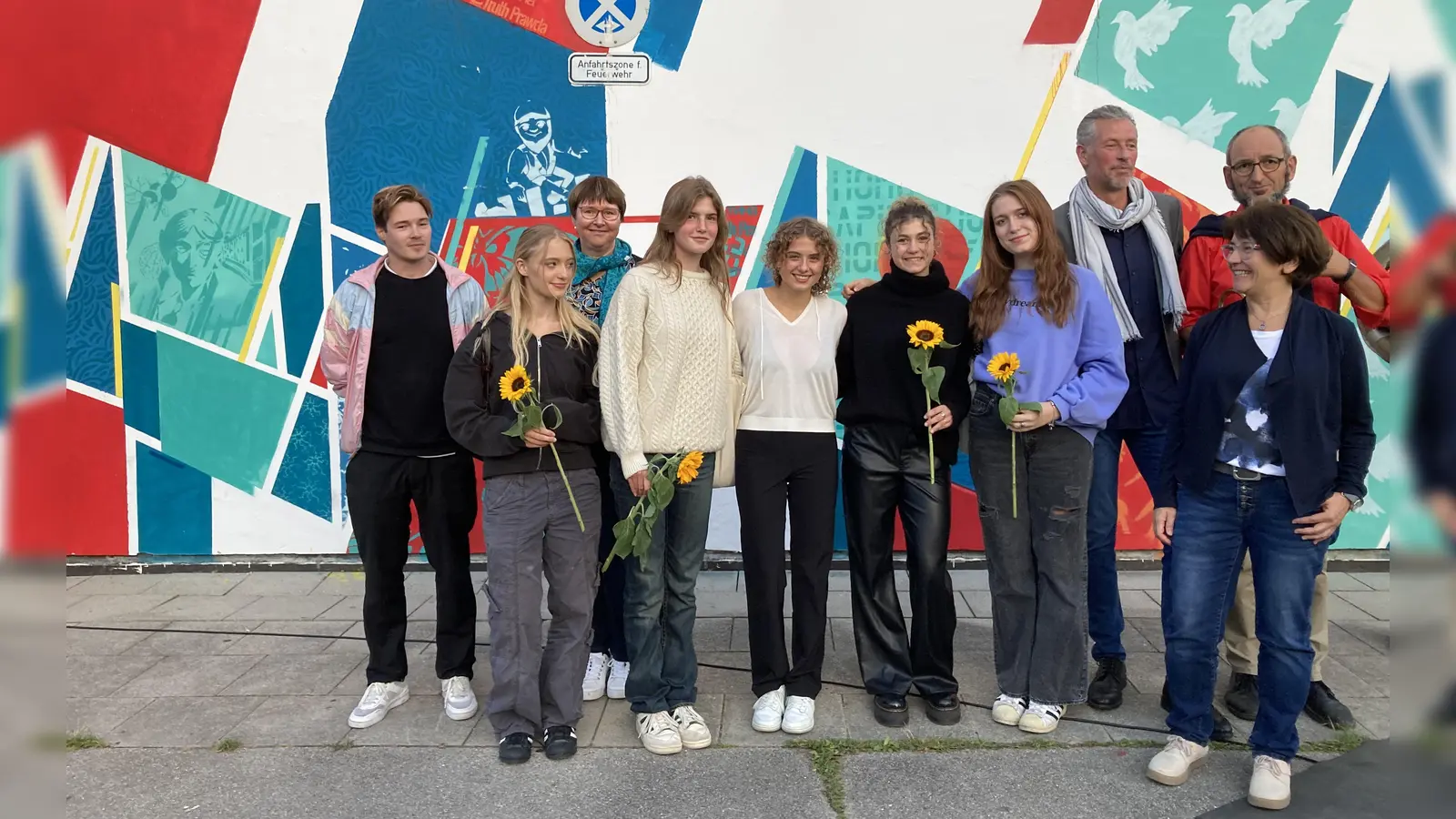 Stolze Fassadengestalter bei der Vernissage, im Bild von links: Künstler Gerald Jegal, Schülerinnen Käthe-Kollwitz-Gymnasiums und Kunstlehrerin Christine Görner-Fliß. Im Hintergrund: Die Elternbeiratsvorsitzende Hilke Derfler, Schulleiter Gerhard Tietz und Leiter der Brassband Alois Schmelz . (Foto: Yvonne Marcuse)