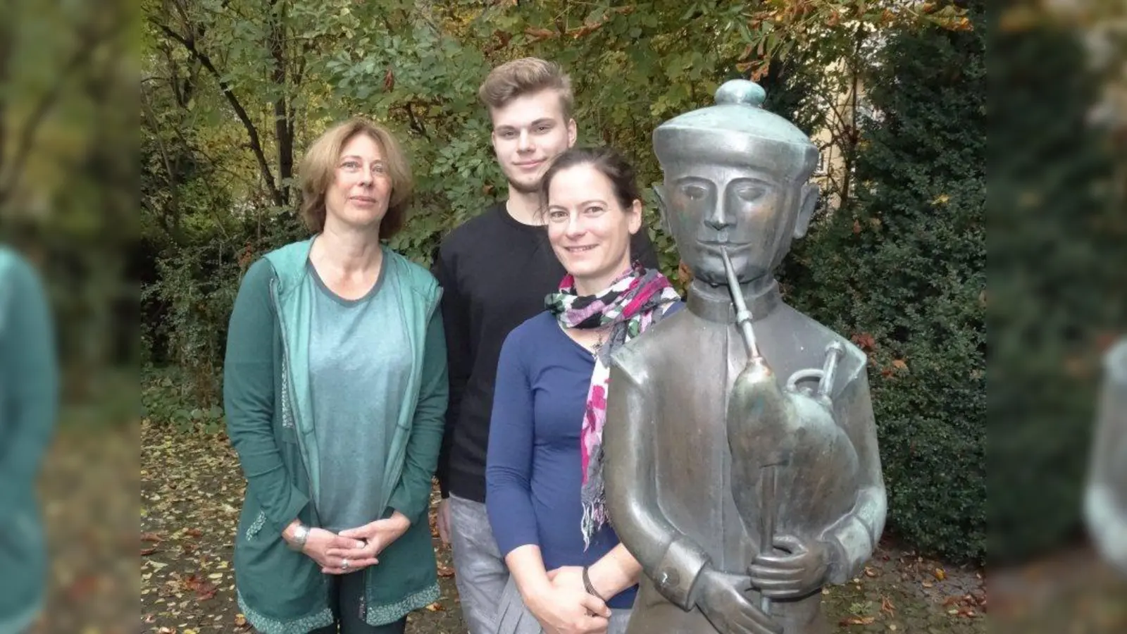 Camilla Meier-Stuckenberger, Leiterin der Personalabteilung bei der AWO München-Stadt, Azubi Janik Woldt und Monika Plass, stellvertretende Leiterin der Personalabteilung bei der AWO München-Stadt (von links), neben der Figur eines Dudelsackbläsers im Hinterhof der AWO-Geschäftsstelle in München. (Foto: tab)