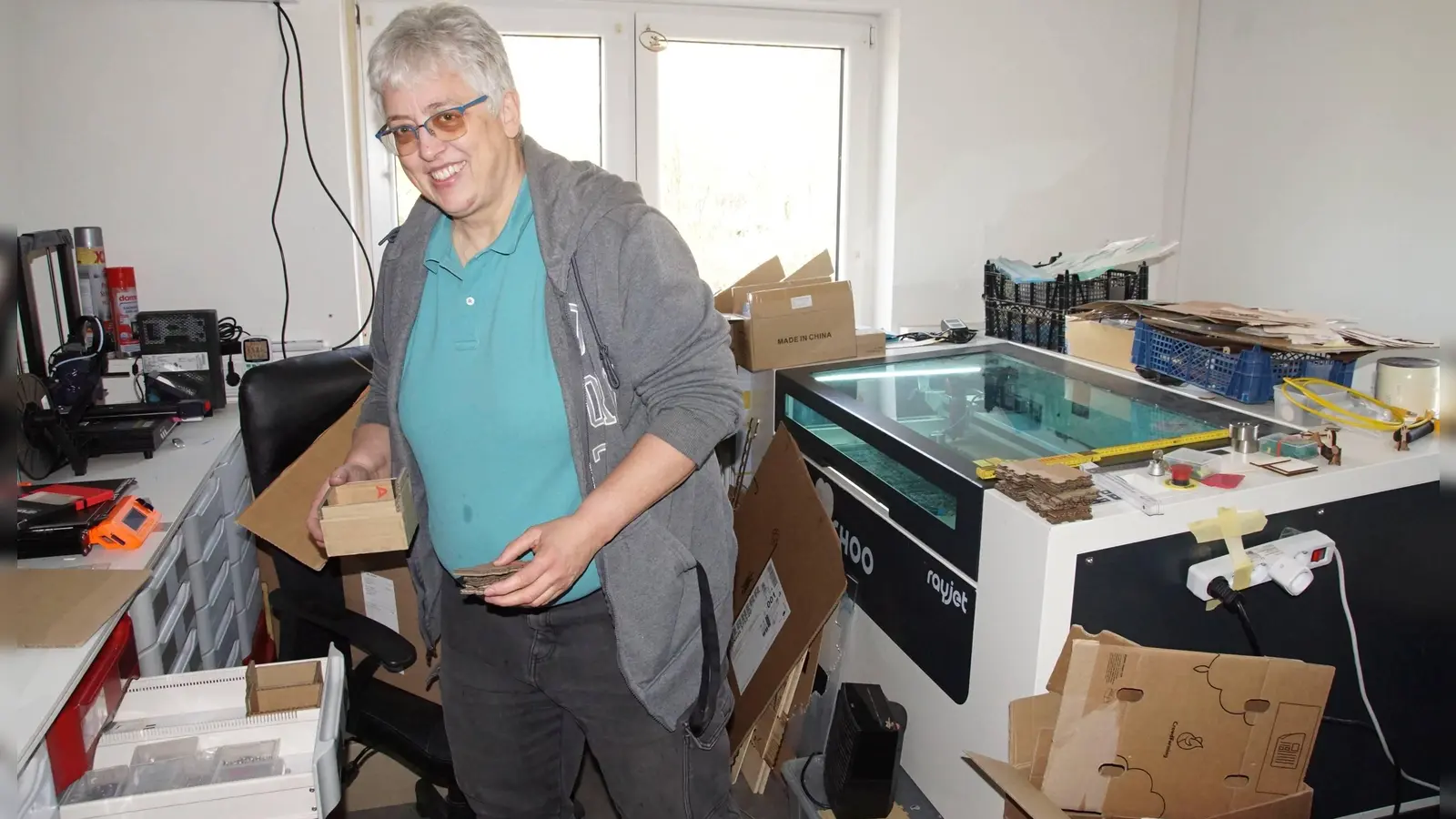 FabLab-Vorsitzende Britta Feldner zwischen Lasercutter und 3D-Drucker mit einem Schächtelchen für Kleinteile in Schubladen. (Foto: bro)