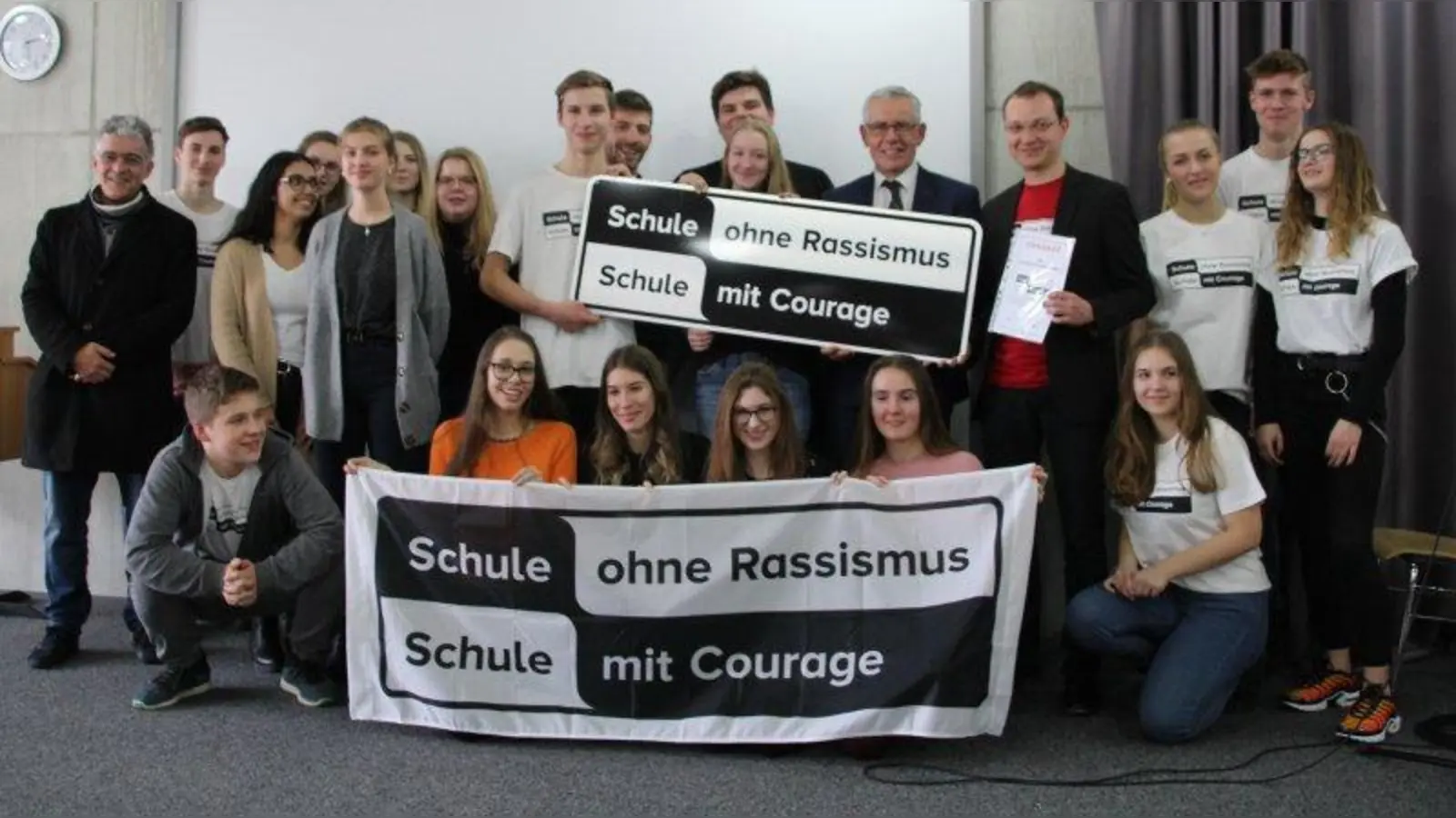 Stolz präsentieren die Teilnehmer des P-Seminars &amp;quot;Schule ohne Rassismus&amp;quot; das entsprechende Schild, das Schulleiter Peter Meyer und Seminarleiter Dr. Stefan Grüner (Fünfter und Vierter von rechts) von Michael Schneider-Velho (links) offiziell für die Schule entgegennahmen. (Foto: mka)