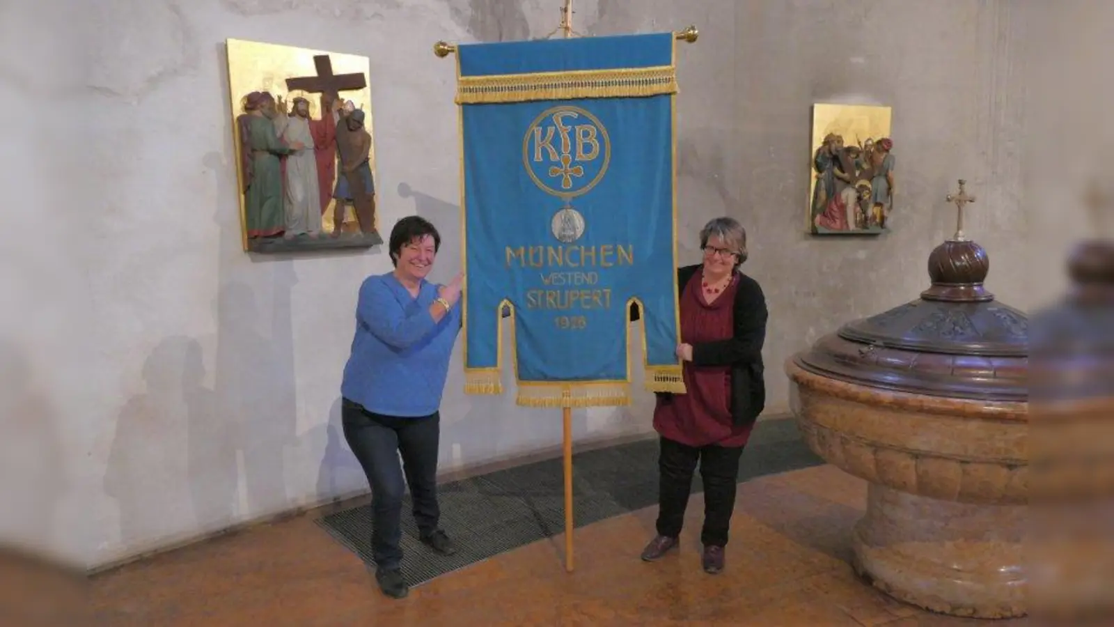 Annemarie Auer (rechts) ist seit zwölf Jahren Vorsitzende der kfd St. Rupert, die am Sonntag, 16. Dezember, ihr 100-jähriges Bestehen groß feiert. Zusammen mit Gemeindereferentin Elisabeth Stanggassinger hält sie das Banner aus dem Jahr 1926 hoch. (Foto: ds)