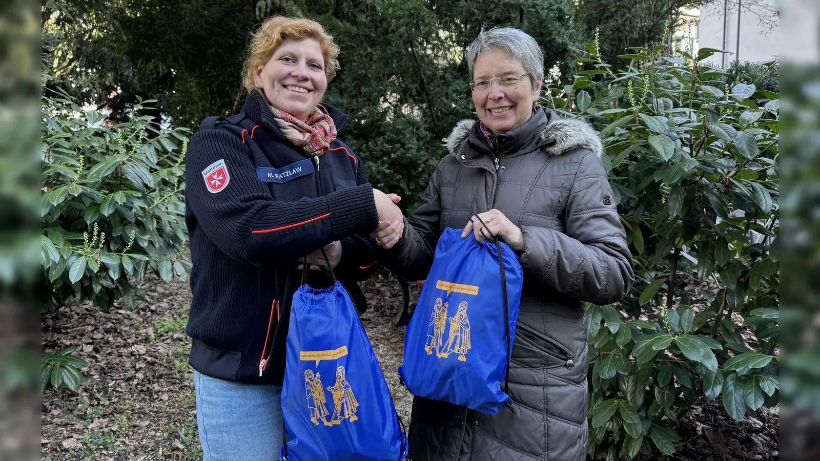 Barbara Massion (l.) von der Dt. Jakobusgesellschaft überreicht Martina Watzlaw Rucksäcke für den Pilgerweg. Geeignet ist die Tour auch für demente Teilnehmer. (F: Silberbauer)