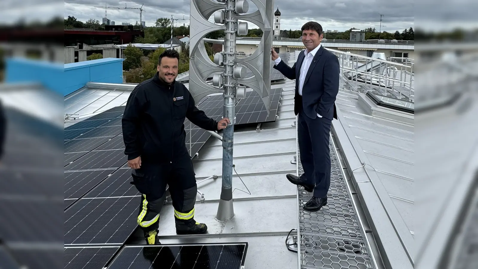 Florian Klietsch (Sachgebietsleiter Öffentliche Sicherheit und Ordnung, Brand- und Katastrophenschutz) und Unterföhrings Bürgermeister Andreas Kemmelmeyer (rechts) begutachten die neue Sirene auf dem Dach der Grundschule an der Bahnhofstraße. (Foto: Gemeinde Ufg/bäu)