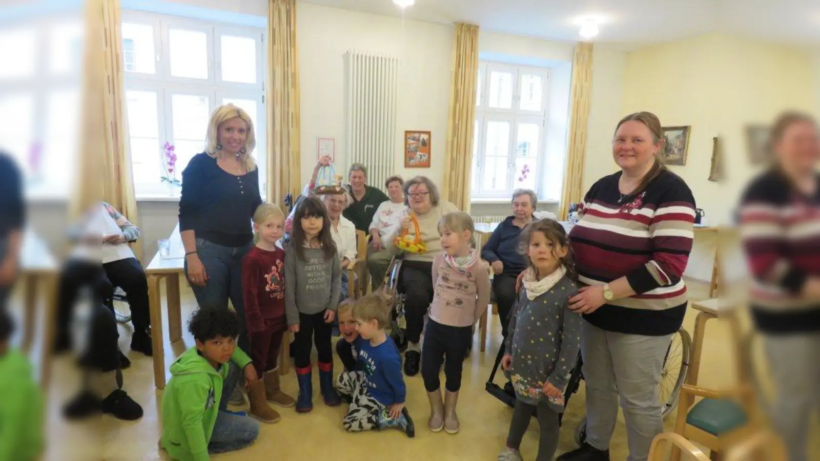 Besuch im Altenheim: Die Kinder hatten gemeinsam mit den Erzieherinnen vor dem Osterfest Osterlämmchen gebacken und Eier gefärbt und diese als Geschenke für die Altenheimbewohner mitgebracht. Auf dem Foto sind die stellvertetende Kiga-Leitung Mihaela Slovova (l.) und Kinderpflegerin Tina Hampl (r.), Josef Hinreiner von der Tagespflege Heilig Geist (hinten m.) mit Kindergartenkindern und Senioren zu sehen. (Foto: Altenheim Heilig Geist)