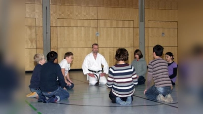 Nachdem sich die Schülerinnen und Schüler kurz in der Turnhalle ausgetobt haben, sammeln sie sich zum Beginn der Karatestunde mit ihrem Trainer zu einer Konzentrationsübung im Kreis. (Foto: Eva Schraft)