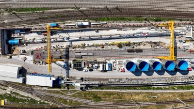 Drohnenaufnahme des westlichen Tunnelportals mit der Tunnelbohrmaschine (das „kleine Blaue” links in der Mitte und der „lange Schwanz” dahinter) in der Startbaugrube. (Foto: DB InfraGO AG / panterralt)