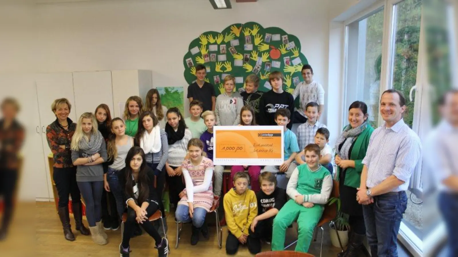 „Wir sind ein Team!” Die jetzige 6a mit Klassenlehrerin Gabriela Marko (l.) vor ihrem Händebaum. Rechts im Bild Interhyp-Mitarbeiterin Patrizia Difonzo und  Projekt-Initiator Andreas Büchl. (Foto: US)