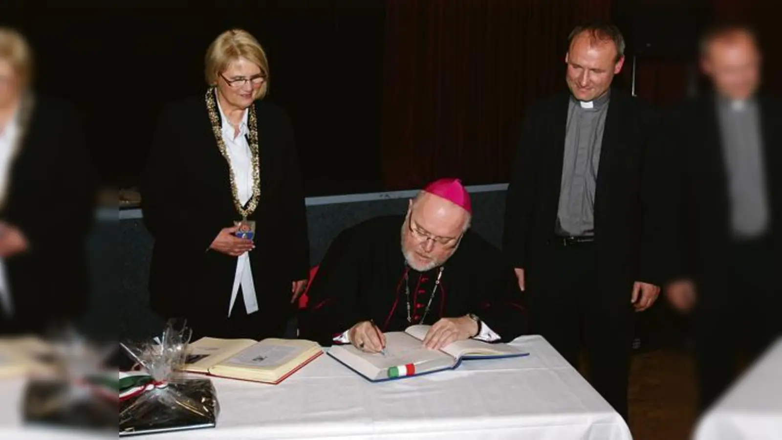 Erzbischof Reinhard Marx trägt sich in das Goldene Buch der Stadt Garching ein, stolz eskortiert von Bürgermeisterin Hannelore Gabor und Pfarrer Bodo Windolf.  (Foto: ba)