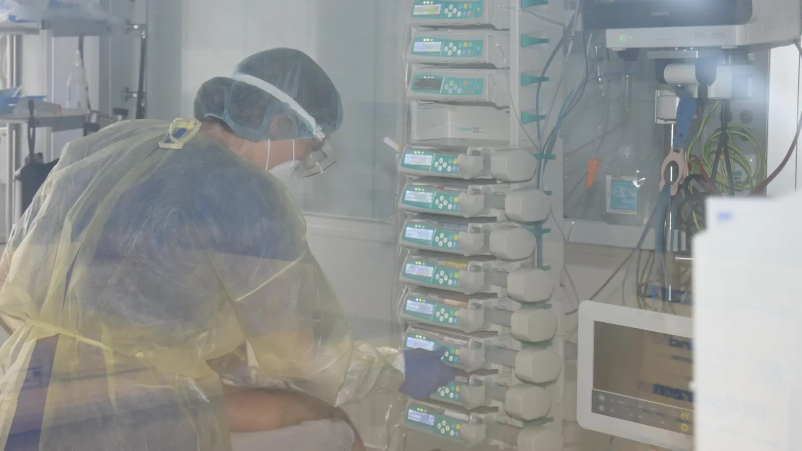 Debora Behrends versorgt hinter einer Schutzscheibe aus Glas einen Corona-Patienten auf der Intensivstation der Kreisklinik Ebersberg. Um sie und andere Pflegefachkräfte zu entlasten, werden ehemalige Pflegekräfte und Medizinstudenten gesucht. (Foto: Kreisklinik)