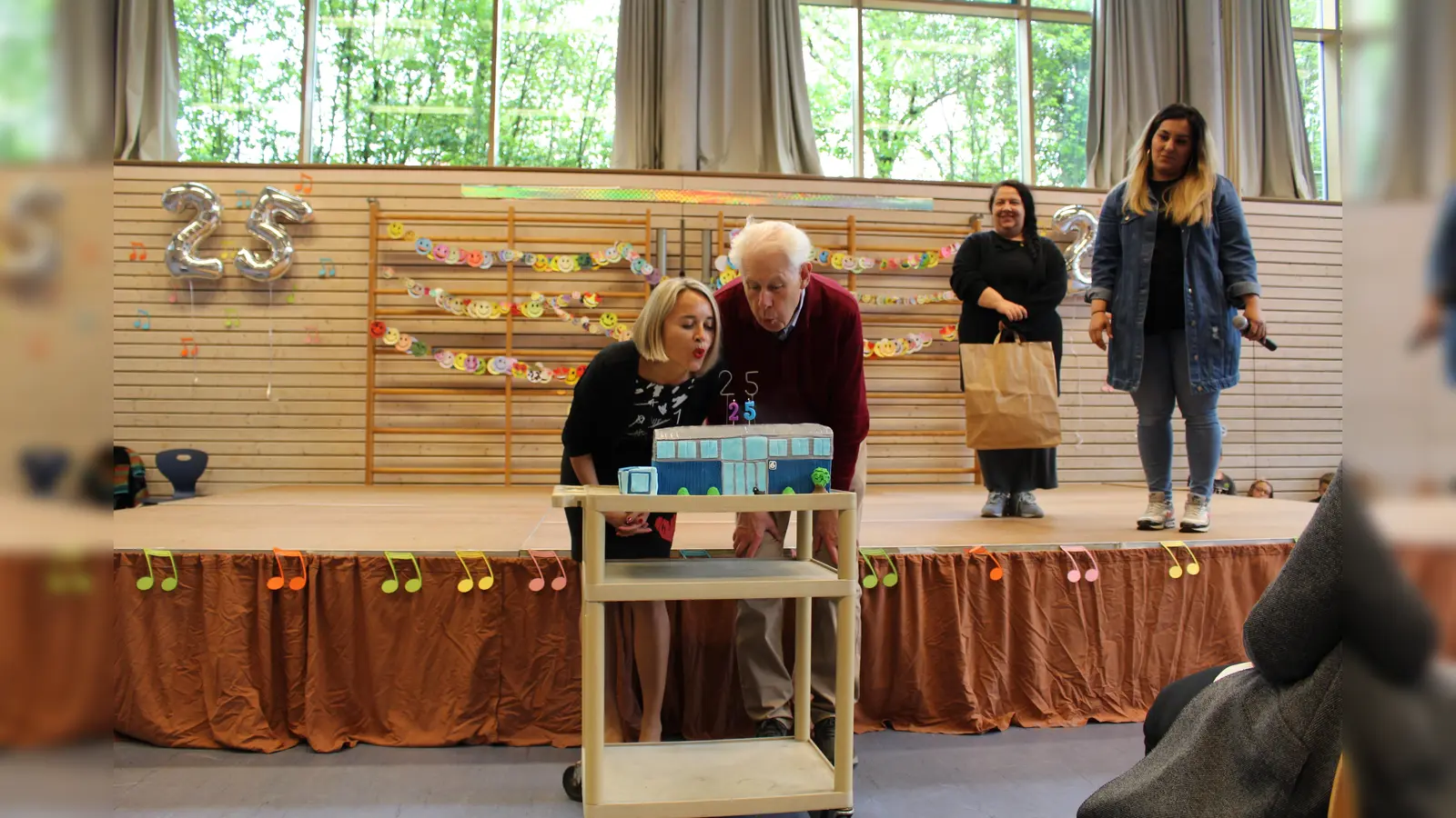 Der Elternbeirat hat der Schule zum Geburtstag einen Kuchen in Form des Schulhauses gebacken. Frau Hofmann und Herr Simon dürfen die Kerzen auspusten. (Foto: VA)