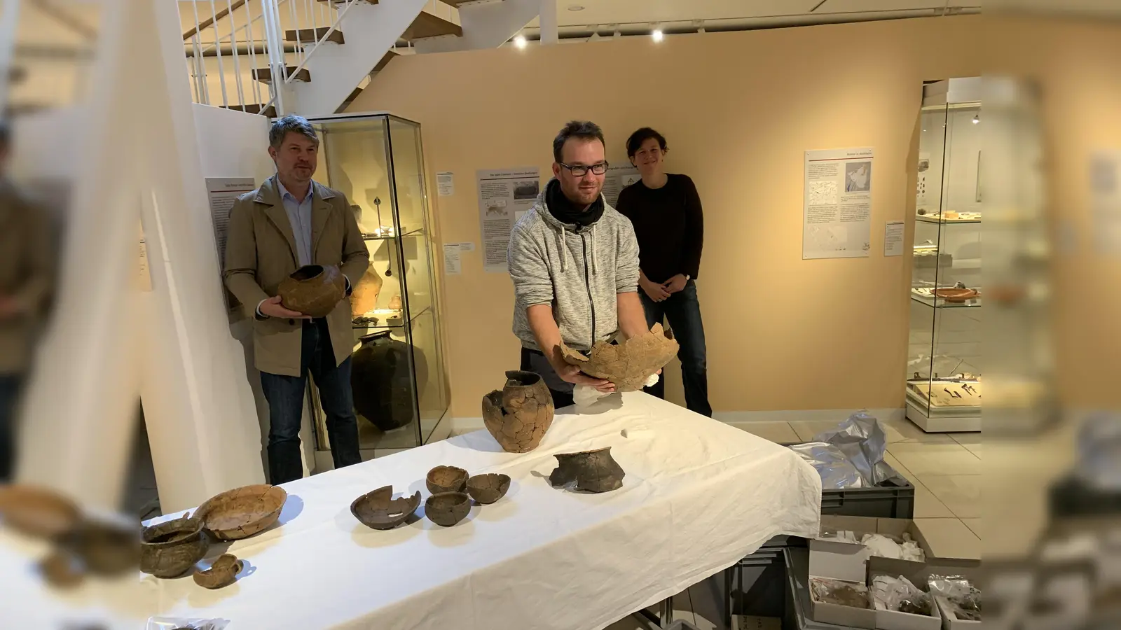 Der "Ausgräber", Carl Göderz von der Firma 3Archäologen, zeigt die neuesten Funde aus Aschheim: Grabbeigaben aus der frühen Eisenzeit. Links Aschheims Erster Bürgermeister Thomas Glashauser, hinten Anja Pütz, Leiterin des AschheiMuseums. (Foto: AschheiMuseum)