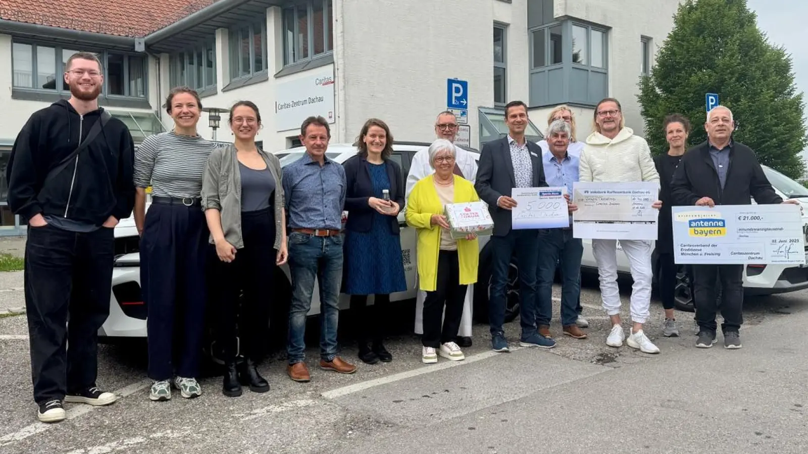 Holger John, Stephanie Wollrab (Stiftung Antenne Bayern), Frank Menauer, Günther Rauch (Löwenkinder e.V.), Anton Limmer (im Hintergrund), Jürgen Vogt (Sparda Bank), Diakon Raimund Richter, Dagmar Krumpach (Sparkasse Dachau), Heidi Schaitl, Andreas Miller, Paola Palmieri, Kathi Köstler, Tom Deschler (alle Caritas-Zentrum Dachau) vor den drei weißen Elektroautos (von rechts). (Foto: Caritas)