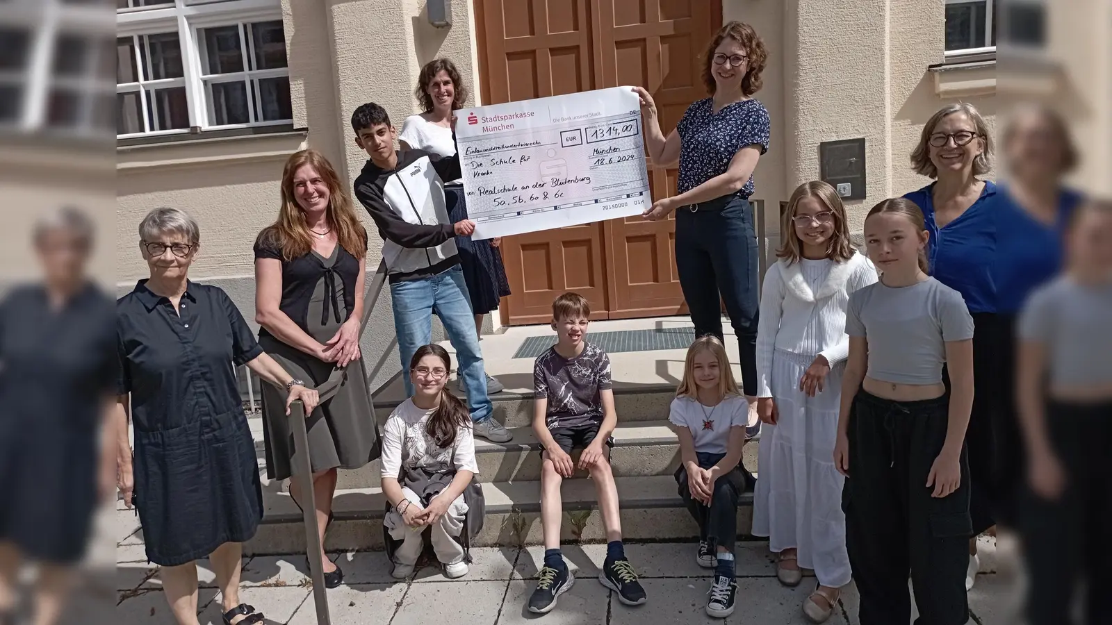 Übergabe des „Vokabel-Schecks” mit Schülerinnen und Schüler der 5. und 6. Klassen sowie Doris Basenach (stellvertretende Schulleiterin, links), Beate Stohl (Lernhausleiterin, Zweite von links), Cordula Steidle (Lernhausleiterin, rechts) sowie Christina Schnös (Lehrkraft und Projektleiterin, hinten links) und Marion Schäfer (Staatliche Schule für Kranke, hinten rechts). (Foto: LHM)