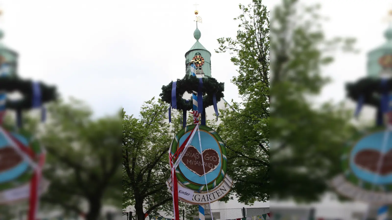 Ein Maibaum mit Bändern und einem bayerischen Gruß schmückte das Maifest vor dem Hintergrund der katholischen Kirche „Mariä Heimsuchung”. (Foto: tg)