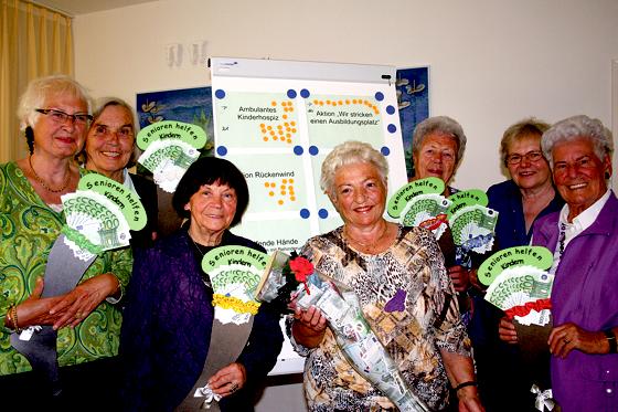 Stricken für den guten Zweck: Sieben Frauen präsentieren sich vor einem Plakat, auf dem die sieben Einrichtungen aufgelistet sind, die jeweils 1000 Euro durch die »strickenden Seniorinnen« erhalten haben. 	Foto: ws
