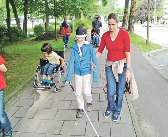 Eren versucht mit »seinem« Rollstuhl voranzukommen, und muss sich dabei ganz schön plagen. Der »blinde« Erasmus wird von seiner Lehrerin Claudia  Karmann auf den rechten Weg gebracht. Foto: hgb