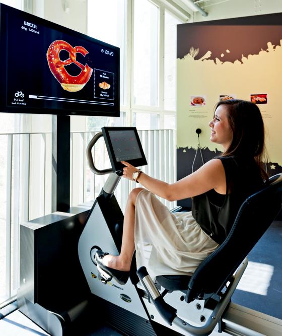 Auf dem Kalorien-Fahrrad kann man sich auf einem Monitor ein Lebensmittel aussuchen, auf das man Appetit hat und dann darf man so lange radeln bis man die virtuell verzehrten Kalorien wieder abgestrampelt hat. Foto: Deutsches Museum