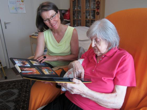 Eine ehrenamtliche Helferin betrachtet zusammen mit einer Seniorin Familienbilder in einem Fotoalbum. 	Foto: Stephan Zöller/M. Bildungswerk