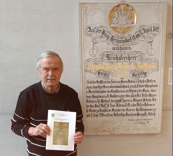 Karl-Heinz Zenker mit dem neuen Sammelblattband vor der Gedenkplatte des Freiherrn von Hallberg, die im Foyer des Rathauses hängt. Foto: Privat