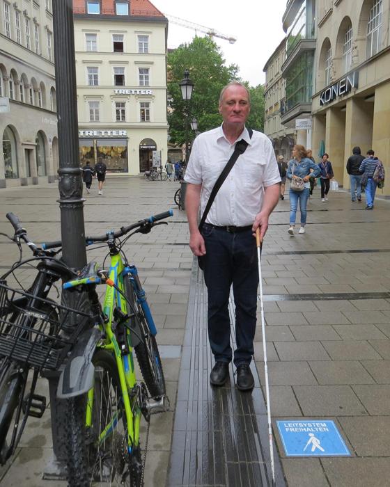 Bernhard Claus, Mitarbeiter für Barrierefreiheit beim BBSB in der Sendlinder Straße am Blindenleitsystem mit Aufkleber.  Foto: © BBSB